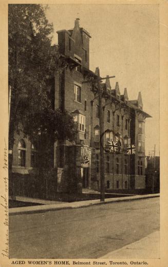 Black and white photograph of a four story public building. Union Jacks are hanging from the wi…