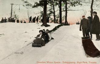 Colorized photograph of a group of three people tobogganing down a hill while others look on.