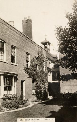 Black and white photo postcard depicting the exterior side wall of a hospital with a chimney an…