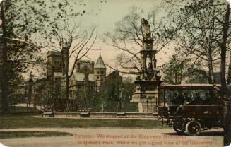 Colour photo postcard depicting a concrete monument with the Queen's Park building depicted in …