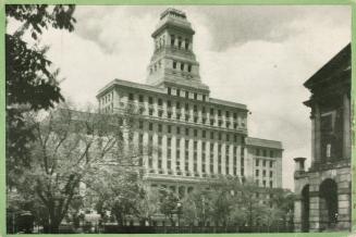 Black and white photograph of a huge Beaux Arts building with trees on the street in front of i…