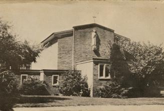 Black and white photo postcard depicting the front of a church with a statue of a saint and a c…