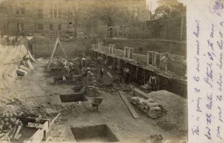 Black and white photograph of a work crew taking wheel barrows of debris away from a demolished…