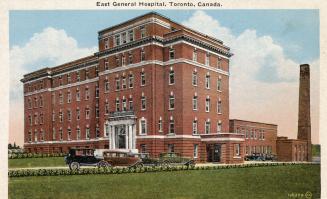 Colorized photograph of a large, square hospital building with three cars parked in front of it…