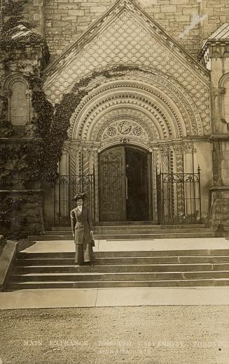 Black and white photograph of a huge, highly stylized, stone doorway. A woman is standing on th…