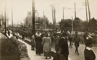 Black and white photograph of soldiers in uniform marching along a street with civilians lookin…