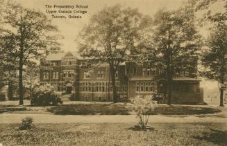 Sepia toned photograph of a large, five story collegiate gothic building in a wooded area.