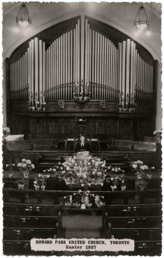 Black and white photo postcard depicting the interior of a church with a minister standing at t…