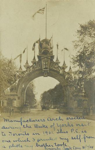 Black and white photograph of a large stone arch spanning a paved road with people and carriage…