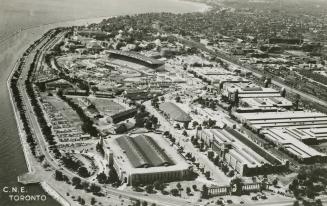 Black and white, aerial shot of large buildings beside a body of water.