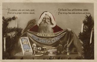 Sepia toned photograph of Santa standing behind a table with toys on it. Greenery with candles …