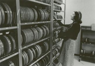 Picture of a woman shelving films on a large shelf full of films. 