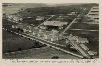 Black and white photo postcard depicting an aerial view of several two-story row buildings in a…