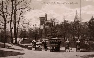 Black and white photograph of people in a horseless carriage waiting at a gate with four pillar…