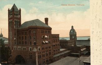 Colour photo postcard depicting an exterior view of Union station, with the entrance arch and t…