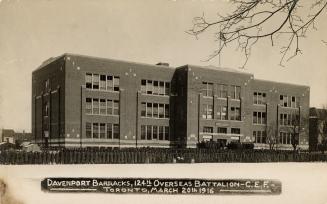 Black and white photo postcard depicting the exterior of a large three-story building with hund…