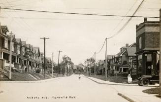 Black and white photo postcard depicting a view looking down a street with a child standing in …