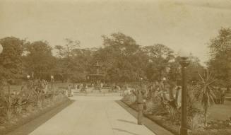 Black and white photograph of a large city garden with fountain at the end of a paved path.