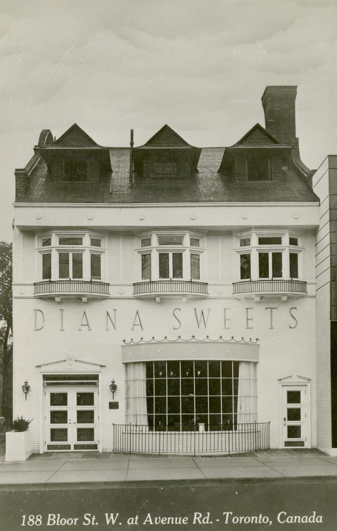 Black and white photo postcard depicting the exterior frontage of a two-story business with the…