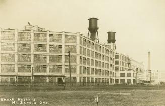 Black and white photo postcard depicting the exterior of two large five-story buildings surroun…