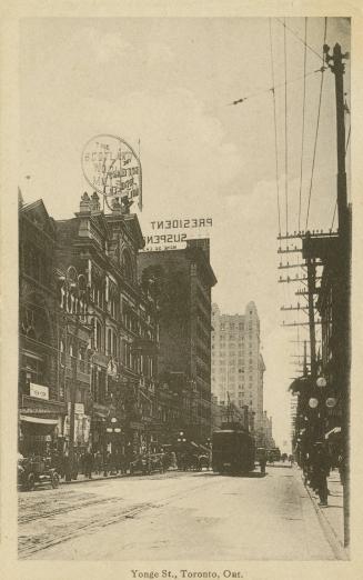 Black and white photo postcard depicting a view of Yonge St. with some buildings, retail shops,…