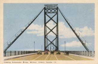 Colorized photograph looking directly across a long suspension bridge. Five automobiles are dri…