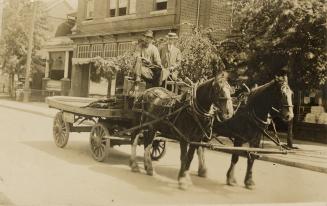 Sepia-toned photo postcard depicting two-men aboard a two-horse-drawn wagon. The back of the ca…