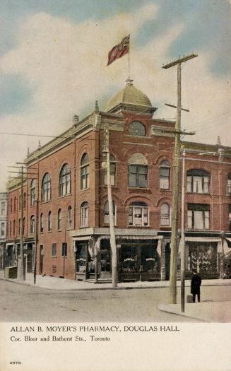 Colour postcard depicting the corner view of a three-story building with flag on its rooftop an…