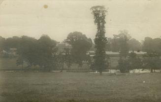 Black and white photograph of a large public building surrounded by water, trees and smaller bu…