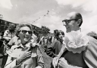 Mr. and Mrs. Robert Stanfield attend a sun drenched neighbourhood fair wearing large paper flow…