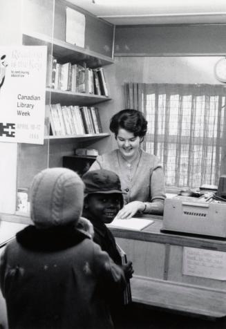 Picture of the interior of a bookmobile with a staff member at a desk with two small children 