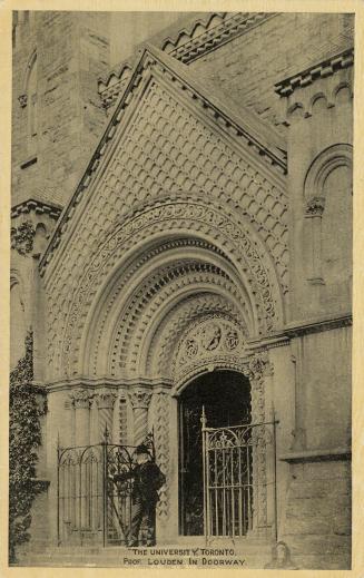 Black and whit photograph of a man standing in front of an elaborate front door to a stone buil…