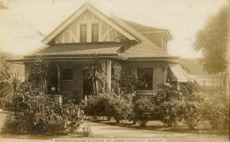 Black and while picture of a cottage surrounded by bushes.