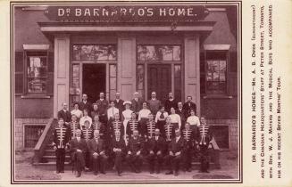 Black and white photograph of a group of adults and boys in uniform posing in front of a large  ...